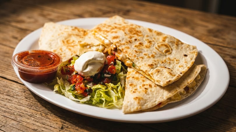 Plate of cheesy quesadillas with salsa, sour cream, shredded lettuce, and pico de gallo on a wooden table.